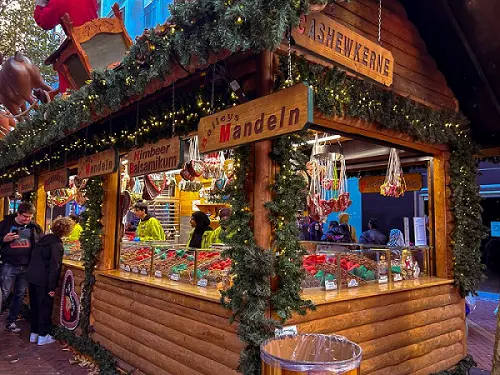 Charming UK Christmas market street with wooden stalls, festive lights, and historic clock tower at dusk.