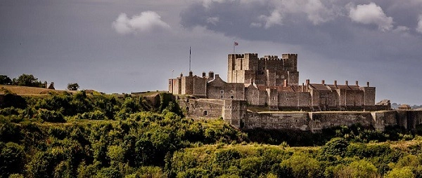 Dover Castle, a grand example of castles in England, stands proudly amidst green hills under a dramatic sky.